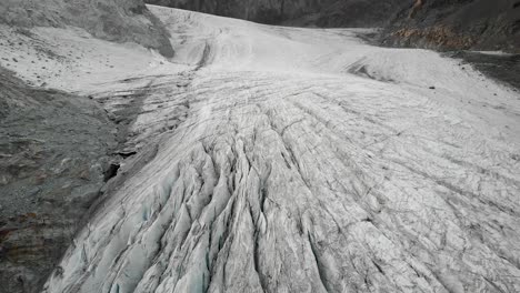 Aerialf-flyover-over-the-ice-and-crevasses-of-Hohlaub-glacier-near-Saas-Fee-in-Valais,-Switzerland-with-a-pan-down-view-towards-the-turquoise-water-of-the-glacial-lake