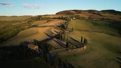 Drone-descends-on-golden-glowing-grass-hills-by-shadows-of-Tuscan-countryside