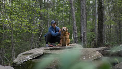 Active-Puerto-Rican-female-petting-family-dog-sitting-on-rock-boulder-in-woodland-forest