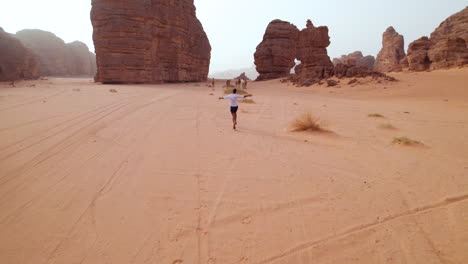 Man-Chasing-Wild-Camels-Running-In-The-Sahara-Desert-In-Tassili-n'Ajjer-National-Park-During-Sunset-In-Africa