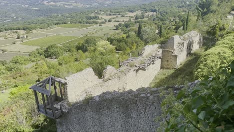 Old-stone-ruin-with-wall-and-growth-in-France-in-front-of-a-wide-forest-landscape-with-forests-and-fields-in-the-distance-to-the-horizon-in-good-weather