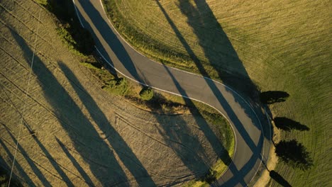 Drohnenübersicht-Von-Oben-Nach-Unten-über-Lange-Schatten,-Die-Landwirtschaftliche-Felder-Der-Toskanischen-Landschaft-Und-Eine-Kurvenreiche-Straße-überqueren