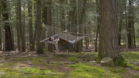 Young-adult-female-swinging-in-hammock-between-woodland-trees-relaxing-and-carefree-life
