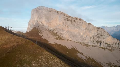 Aerial-flyover-alongside-the-cliffs-of-Tour-d'Aï-and-slopes-of-Leysin-in-Vaud,-Switzerland-with-les-Diablerets-in-view-during-a-colorful-autumn-afternoon-in-the-Swiss-Alps
