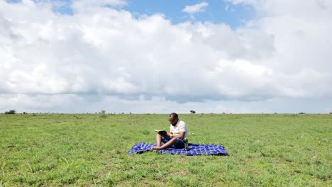 Time-lapse-shot-of-a-black-man-who-sits-on-a-blanket-in-the-grass-taking-notes-in-a-book