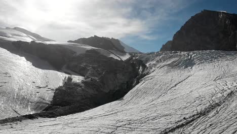 Sobrevuelo-Aéreo-Sobre-El-Hielo-Del-Glaciar-Allalin-Cerca-De-Saas-fee-En-Valais,-Suiza-Con-Un-Excursionista-Disfrutando-Del-Día-Soleado-En-Los-Alpes-Suizos
