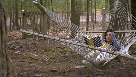 Young-carefree-female-swinging-in-forest-hammock-reading-book-in-peace