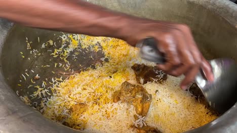 Close-up-shot-of-male-hands-packing-hot-freshly-cooked-biryani-dish-from-large-container-in-a-kitchen
