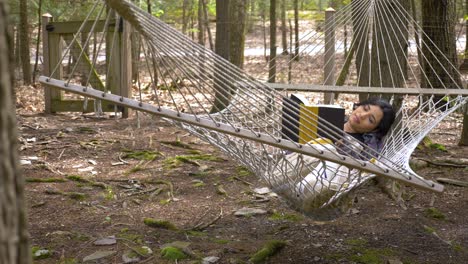 Carefree-young-Caribbean-woman-reading-novel-swinging-in-woodland-hammock