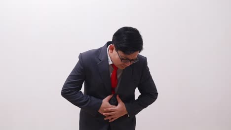 Asian-businessman-in-suit-suffering-from-stomach-ache,-hands-holding-stomach