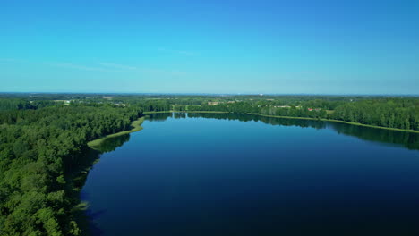Antena-Sobre-Un-Maravilloso-Lago-Natural-Alrededor-De-Un-Bosque-Siempre-Verde-En-Una-Zona-Rural-Durante-El-Día