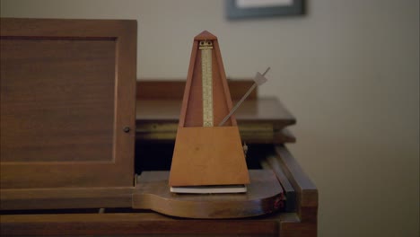 Antique-wooden-vintage-metronome-marks-60-bpm-by-swinging-a-weight-back-and-forth-once-per-second-on-top-of-an-old-piano