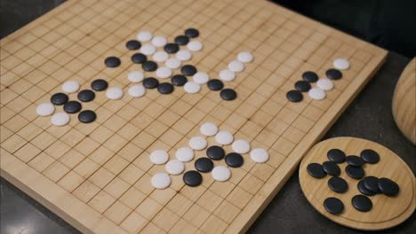 Overhead-45-degree-view-of-man's-hand-placing-a-white-stone-in-the-middle-of-the-ancient-Chinese-board-game-Go-on-a-bamboo-wooden-board-with-black-pieces-scattered-in-the-foreground