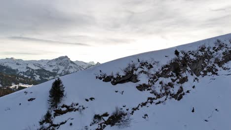 Aufschlussreicher-Flug-Aus-Der-Luft-über-Den-Berghang,-Der-Die-Schneebedeckte-Bergkette-Bei-Sonnenuntergang-In-Amden,-Schweiz,-Zeigt---Nadelbäume-Im-Tal