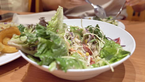 Close-up-of-an-individual-mixing-a-bowl-full-of-vegetable-salad-with-a-spoon-and-a-fork-at-a-restaurant-in-Bangkok,-Thailand
