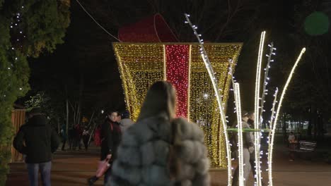 People-Casually-Strolling-in-the-Park,-Surrounded-by-Festive-Lights,-During-Galati-National-Day-in-Romania---Wide-Shot