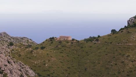 Enthüllen-Sie-Eine-Aufnahme-Eines-Kleinen-Hauses-Und-Einer-Straße-Auf-Dem-Hügelpass-Auf-Der-Insel-Mallorca,-Luftaufnahme