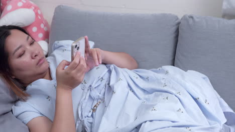 Woman-lying-down-on-a-couch-while-she-is-browsing-her-phone-to-check-her-messages-on-her-social-media