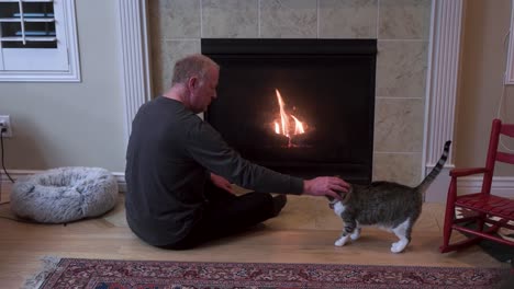 Senior-man-sits-with-his-pet-cat-by-the-fireplace