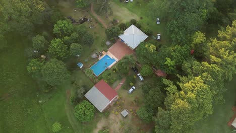 AERIAL-ORBIT-shot-top-down-looking-over-a-farmhouse-with-a-swimming-pool-in-the-center-of-green-lush-trees
