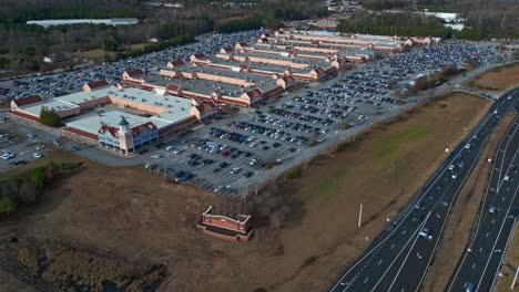 Aerial-wide-shot-showing-crowded-Parking-area-at-Shopping-mall-and-driving-Vehicle-on-highway-in-America
