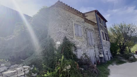 Small-old-stone-farmhouse-in-France-in-the-sun-with-old-windows-overgrown-by-nature-with-a-footpath-in-front-of-it