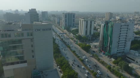 Toma-De-Drone-Paralaspe-Del-Edificio-De-CDC-Al-Lado-De-Una-Carretera-Muy-Transitada-En-Karachi,-Pakistán