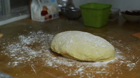 Dry-white-flours-sprinkled-by-hand-over-freshly-risen-dough-ball-on-kitchen-table-top,-filmed-as-close-up-shot-in-slow-motion