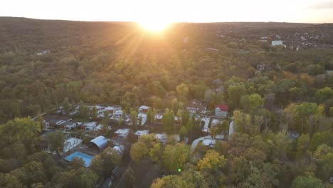 flying-diagonally-on-the-horizon-at-sunset-over-a-town-located-between-trees-in-the-forest-in-autumn