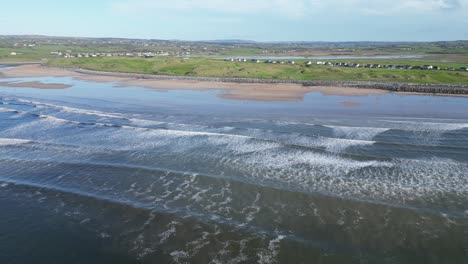 Aerial-descending-shot-of-waves-crashing-at-Lahinch-beach-with-seafront-houses