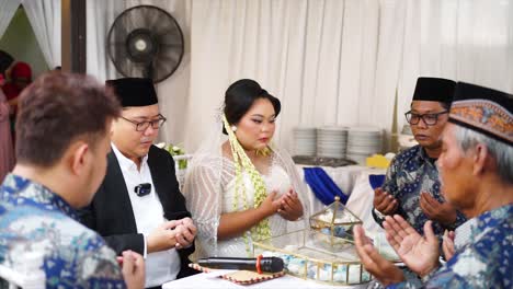 Muslim-bride-and-groom-pray-after-carrying-out-the-marriage-contract-at-an-Indonesian-wedding-celebration-accompanied-by-witnesses,-officiant-and-family