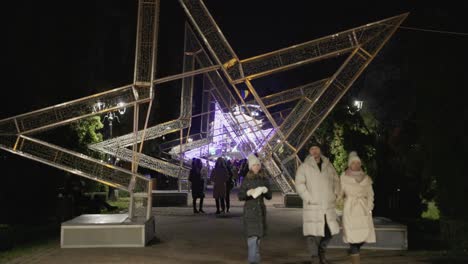 Menschen,-Die-Während-Des-Galati-Nationalfeiertags-In-Rumänien-Unter-Einem-Riesigen,-Mit-Festlichen-Lichtern-Geschmückten-Stern-Im-Park-Spazieren-–-Totalaufnahme