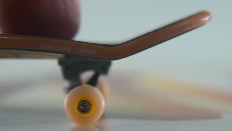 A-hyper-close-up-macro-detailed-shot-of-a-mini-skateboard,-tiny-white-wheels,-riding-fingerboard-from-right-to-left,-finger-slide,-professional-lighting,-static-cinematic-4K-video