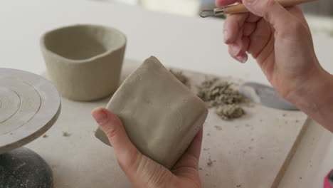 Picking-up-tools-to-masterfully-engrave-intricate-designs-into-soft-clay-showcasing-artisan's-delicate-touch