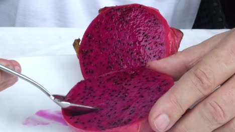 A-closeup-of-a-sliced-dragon-fruit-with-a-man's-hands-scooping-it