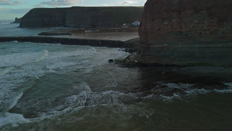 Low-Revealing-Drone-Shot-of-Staithes-from-Behind-Cliff-at-High-Tide-UK