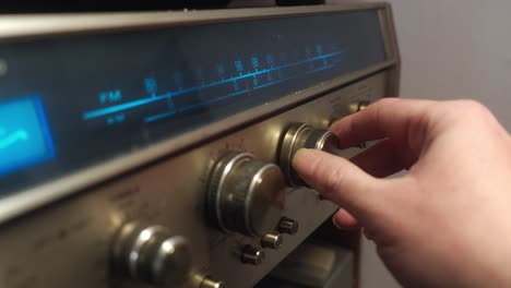 Close-up-of-a-hand-turning-a-knob-to-change-frequency-on-a-retro-radio-with-metal-design-and-blue-backlit-display