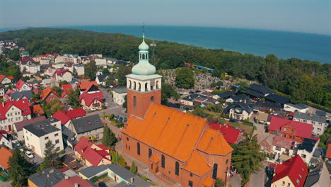 Drone-flying-above-the-church-in-Jastarnia,-Poland-with-baltic-sea-in-the-background