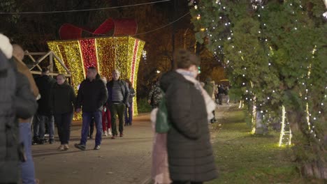 People-Casually-Walking-Through-the-Park,-which-is-Decorated-with-Celebratory-Lights,-on-Galati-National-Day-in-Romania---Wide-Shot