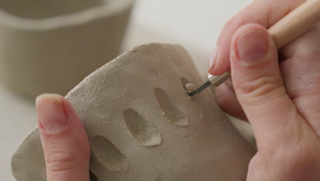 Engraving-intricate-designs-into-soft-clay-with-a-specialized-tool,-showcasing-artisan's-delicate-touch