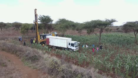 Workers-drilling-machine-boring-hole-for-water-well-on-African-farmland,-aerial-view
