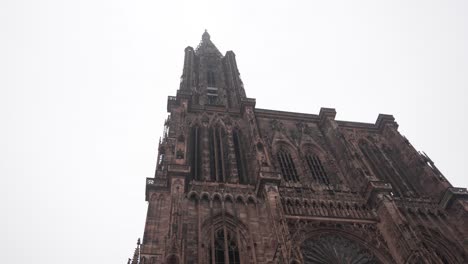 View-onto-the-Strasbourg-Cathedral-against-a-cloudy-sky-backdrop,-the-intricately-carved-facade-beckons,-adorned-with-an-array-of-sculptures-depicting-scenes-from-the-Bible-and-medieval-life