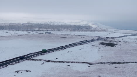 Aerial-Drone-Shot-of-Snowy-Road-in-Yorkshire-Dales-with-Car-and-Van-Passing-by-UK