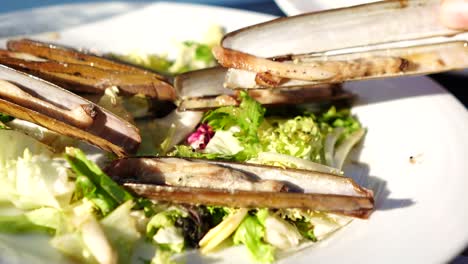 Hand-Nimmt-Gegrillte-Seemuschel-Auf-Weißem-Teller-Mit-Salat