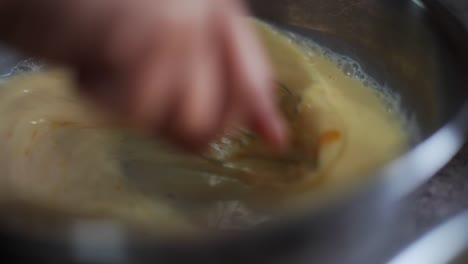 Egg-yolk-and-milk-whisked-and-blended-in-metal-bowl,-filmed-as-closeup-slow-motion-shot