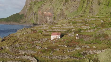 Side-panning-shot-of-old-house-near-sea-at-Flores-island,-aerial