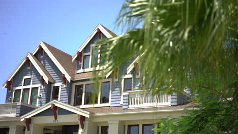 Wohlhabende,-Moderne-Blaue-Holzfassade,-Dachlinie-Hinter-Bokeh-Gartenpalmenblättern