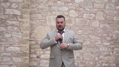 A-groom-walks-confidently-towards-camera-while-adjusting-his-tie-and-looks-at-his-watch-to-check-the-time