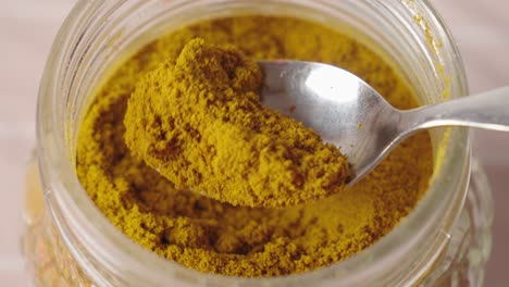 Person-picking-up-a-spoonful-of-dry-curcuma-from-a-spice-jar