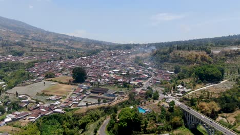 Busy-village-near-massive-mountain-slope,-aerial-drone-view